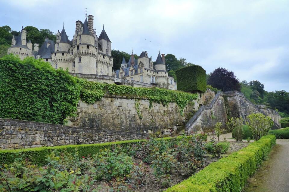 A historic castle with multiple towers and a stone wall with greenery.