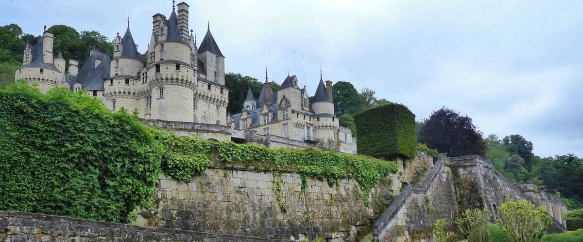 A historic castle with multiple towers and a stone wall with greenery.
