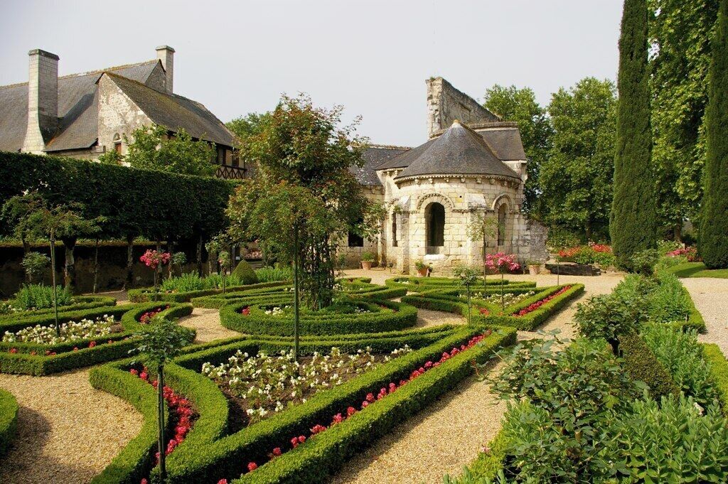 Un jardin à la française, avec des haies aux formes géométriques, une structure centrale en pierre et un grand arbre.