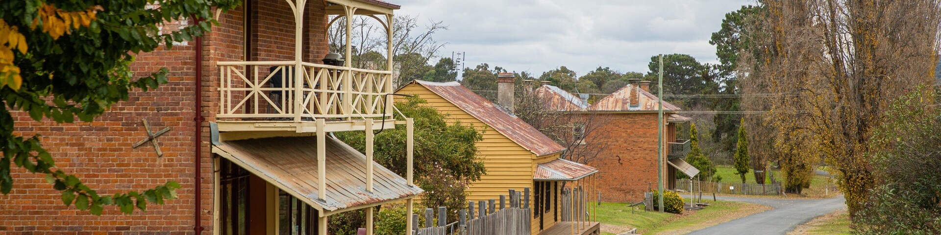 A quiet street lined with traditional brick houses, a wooden fence, and a clear road.
