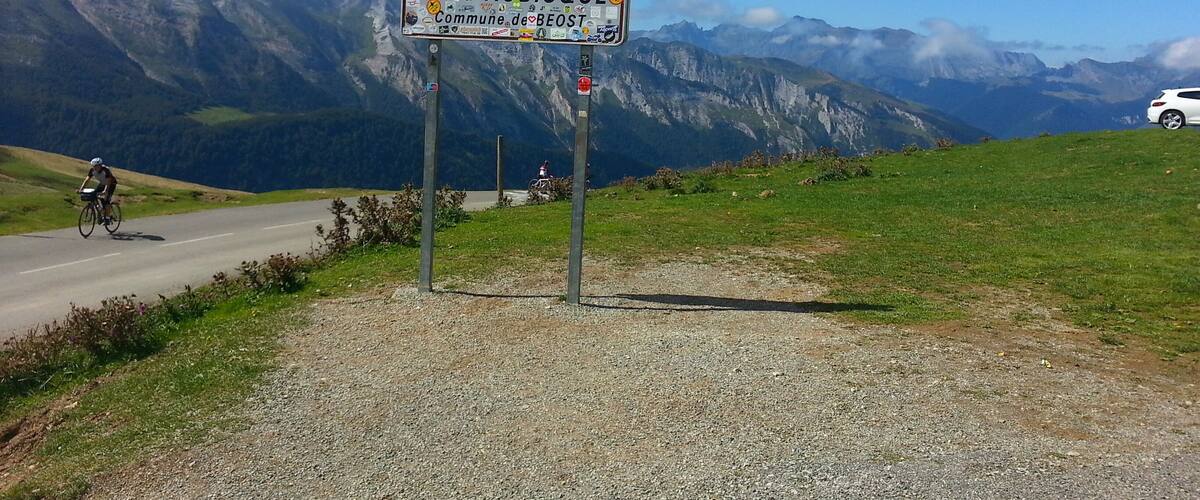 A signpost with stickers, a cyclist, and a mountain landscape.