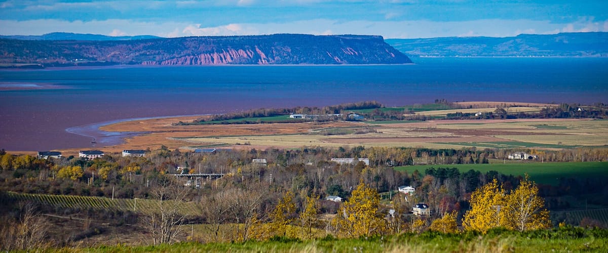 A coastal landscape with a river, farmland, and a distant mountain range.