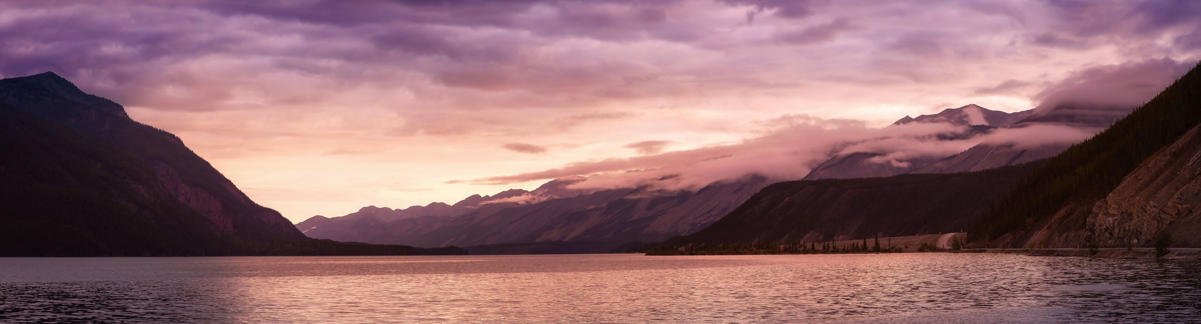 A mountain lake with reflections of the sky, surrounded by forested slopes.