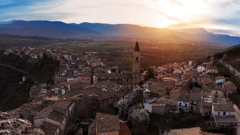 A mountainous town with a prominent church tower, surrounded by terraced houses and a valley.