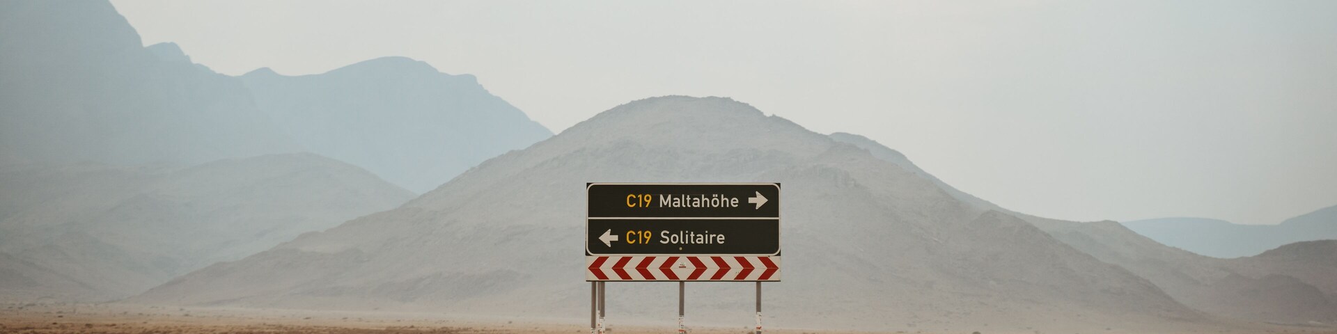 A road sign in a desert landscape with mountains in the background.