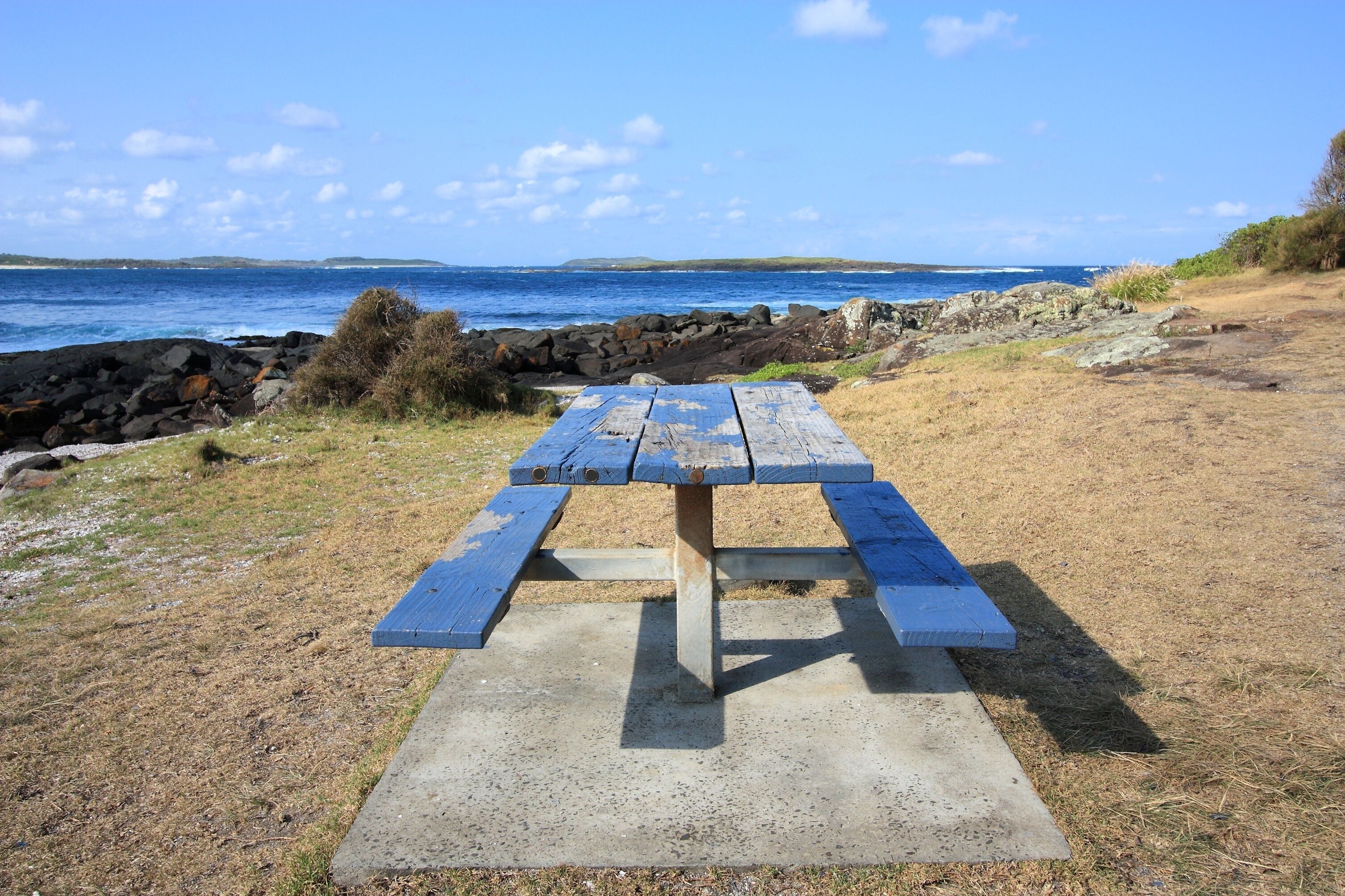 A picnic table by a rocky shoreline with the ocean in the background.