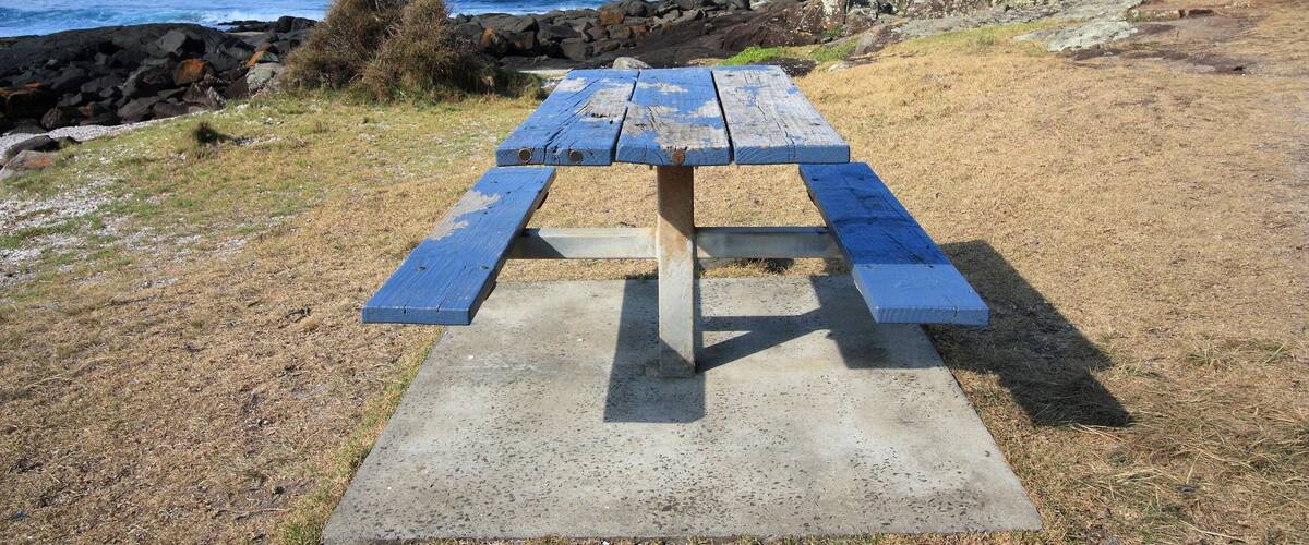 A picnic table by a rocky shoreline with the ocean in the background.