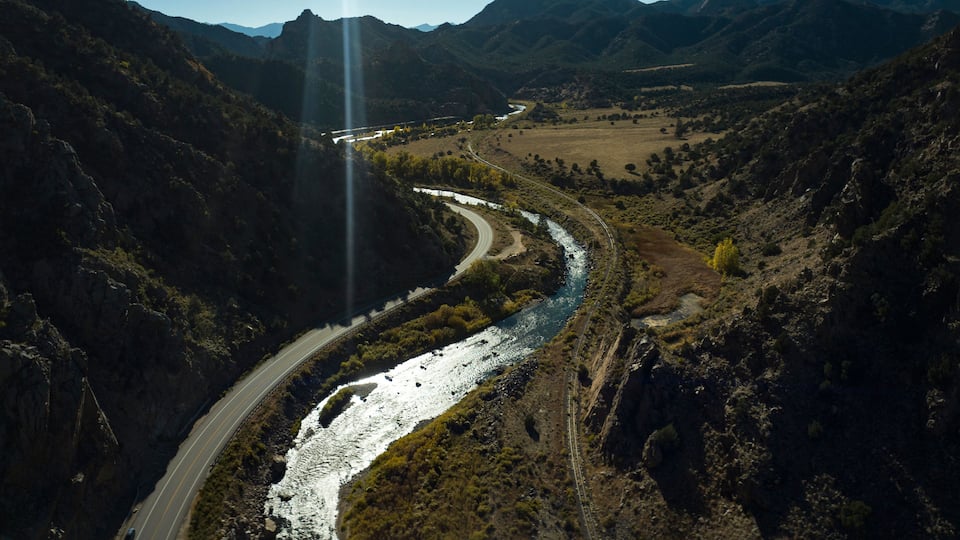 A winding river through a mountainous landscape with a road curving alongside it.