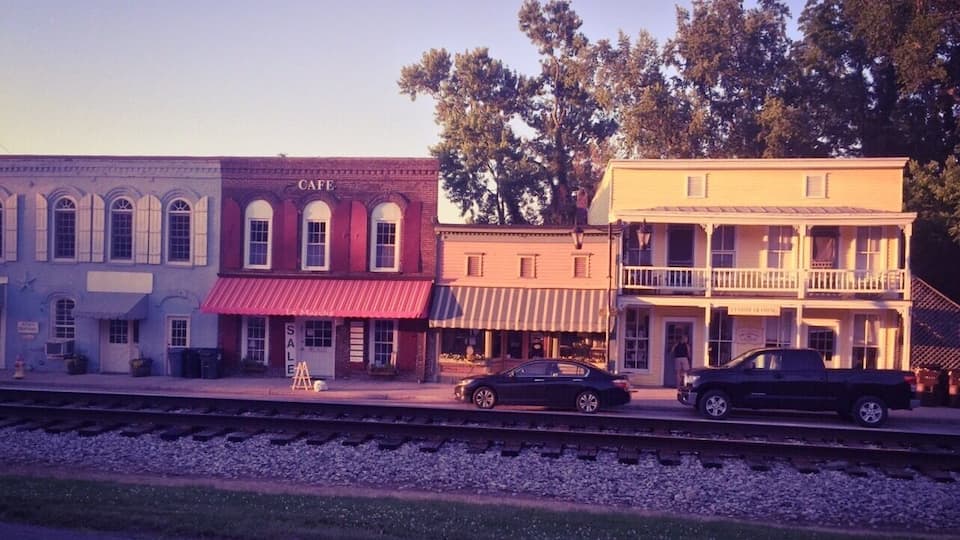 A train station with a cafe, a building labeled 'TESTING TRAINING,' and a black car parked on the platform.