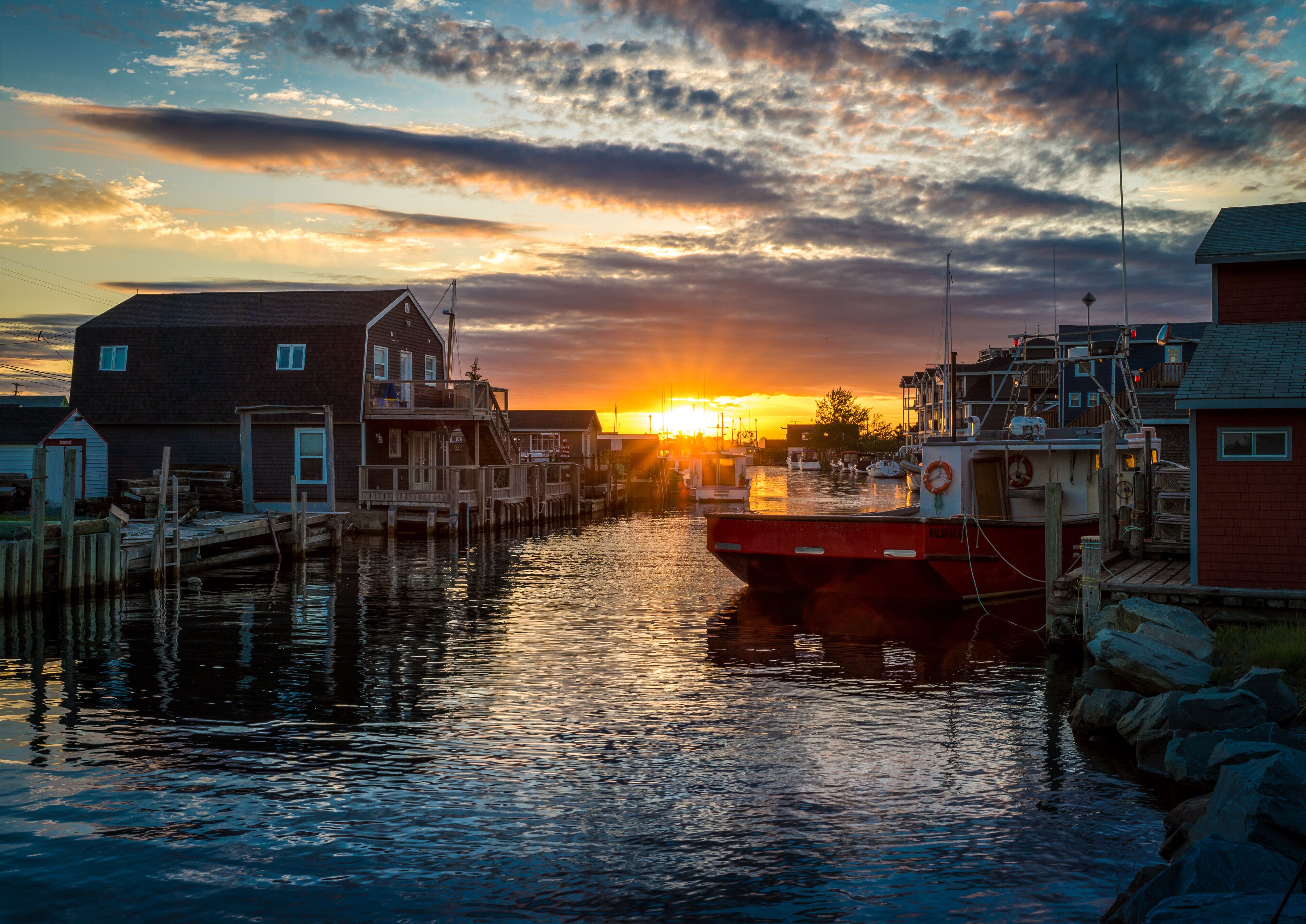A sunset over a harbor with boats, wooden docks, and buildings.