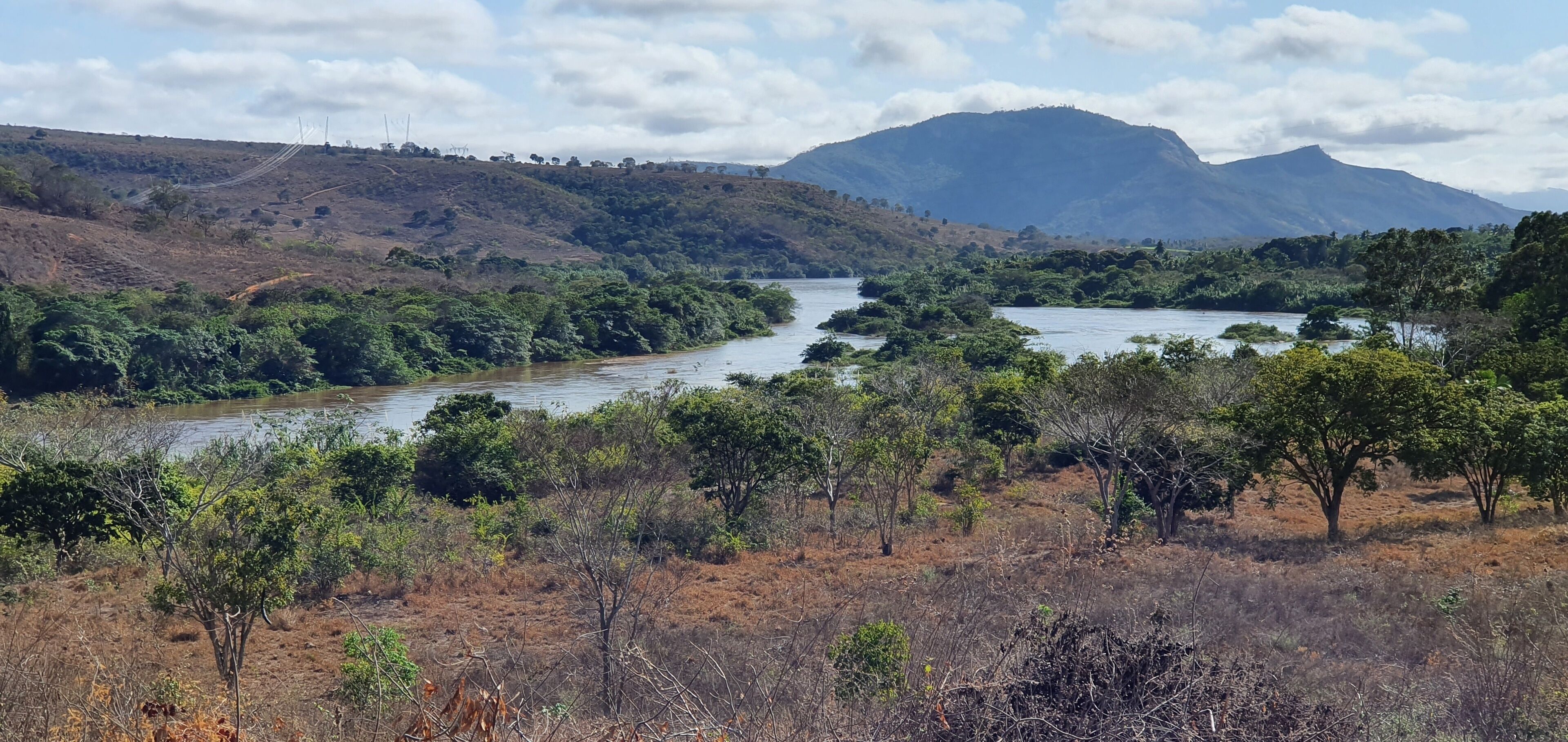 A river winding through a hilly landscape with dense vegetation and a mountain in the background.