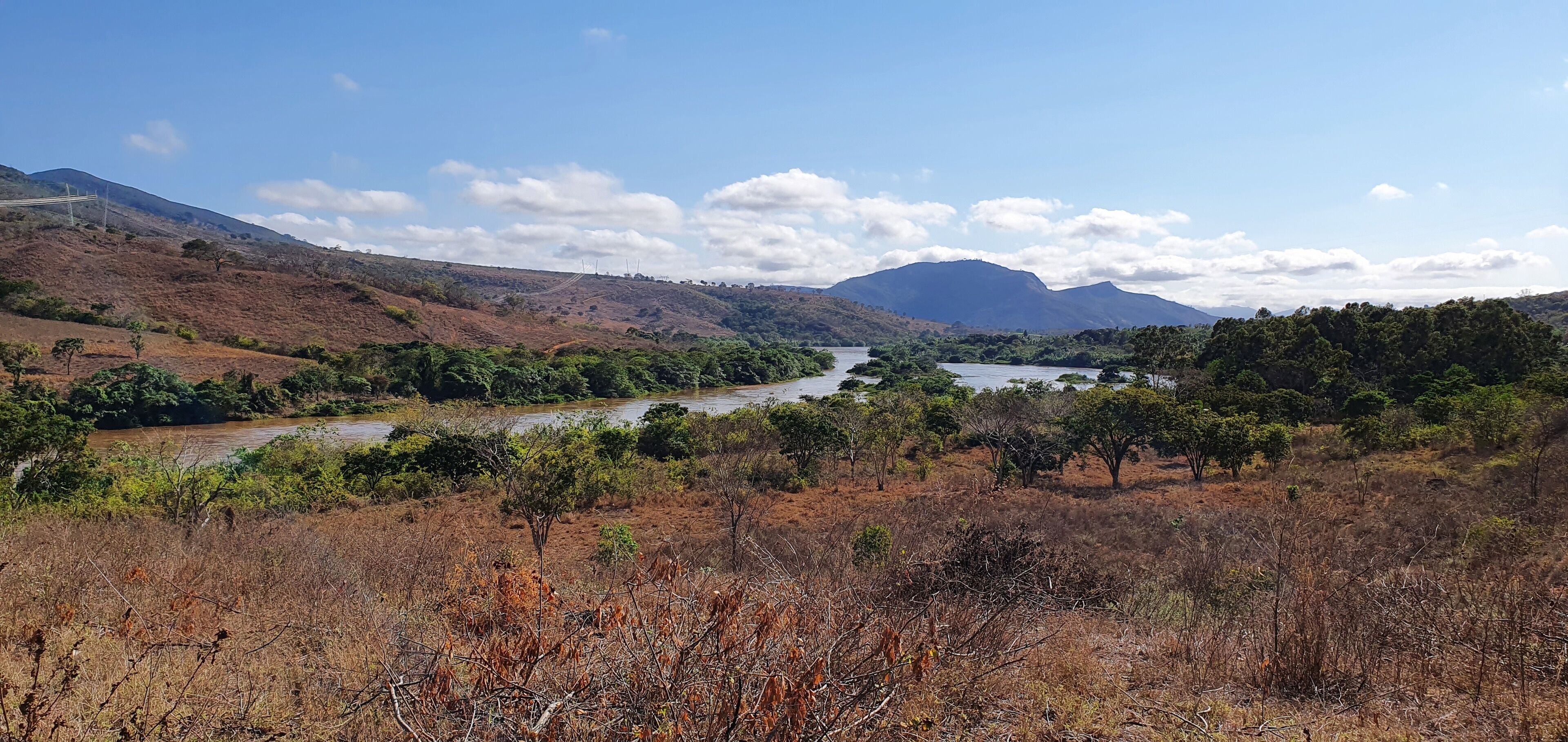 A river winding through a dry, hilly landscape with sparse vegetation and distant mountains under a clear sky.