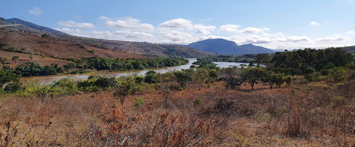 A river winding through a dry, hilly landscape with sparse vegetation and distant mountains under a clear sky.