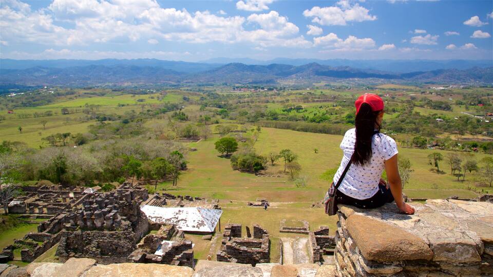 A woman sitting on ancient ruins overlooking a vast landscape with distant mountains.
