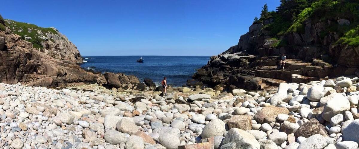 A rocky beach with large boulders and a clear blue sea.