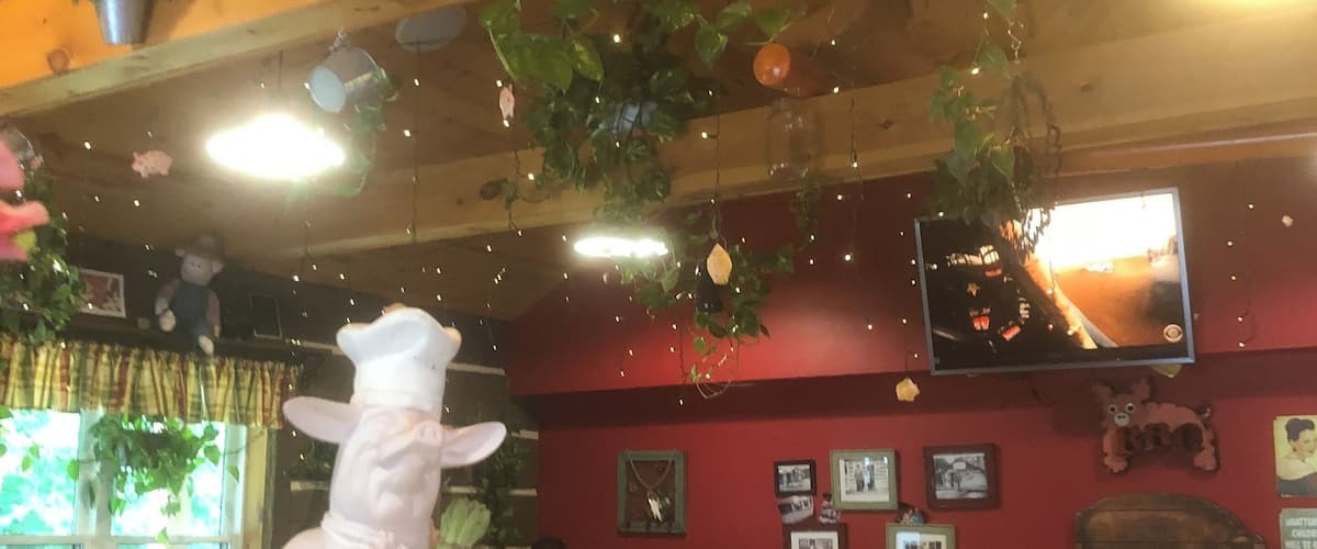 A restaurant interior with wooden ceilings, hanging plants, and a white waiter statue.