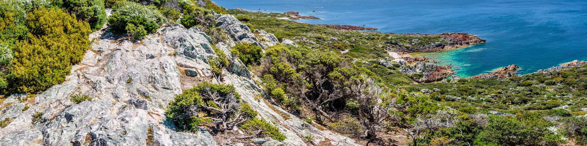Stunning view from bright white light station to deep blue sea ocean bay turquoise water with orange red rocks at shore coast on warm sunny clear sky day, Rocky Cape National Park, Tasmania, Australia