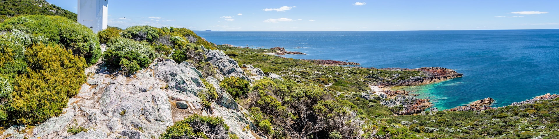 Stunning view from bright white light station to deep blue sea ocean bay turquoise water with orange red rocks at shore coast on warm sunny clear sky day, Rocky Cape National Park, Tasmania, Australia