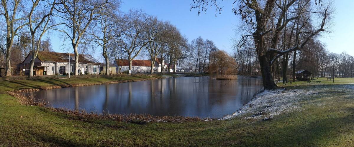 A calm lake with a grassy bank, trees, and a building in the background.