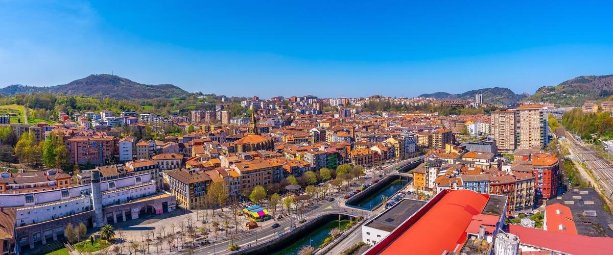 A cityscape with a river, historic buildings, and a mountainous backdrop.