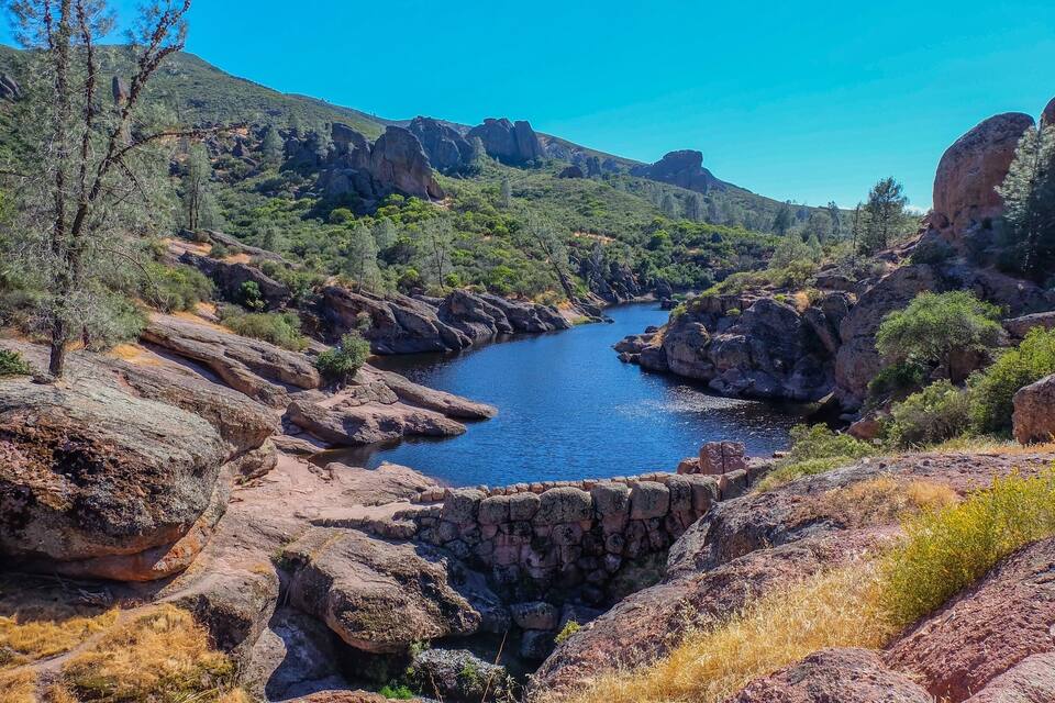 A river winding through a rocky canyon with green vegetation and a clear blue sky.