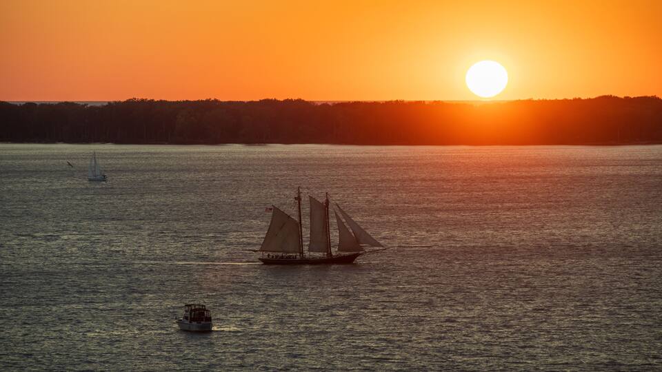 A sailboat on a calm body of water with a sunset in the background.