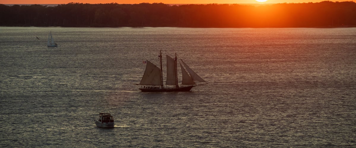A sailboat on a calm body of water with a sunset in the background.