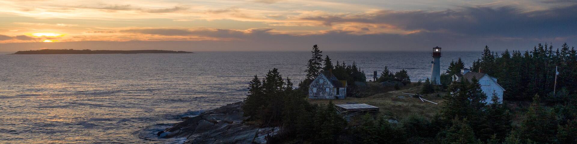 a lighthouse is perched at the edge of a rocky shoreline at sunset