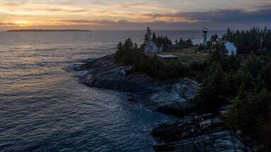 a lighthouse is perched at the edge of a rocky shoreline at sunset