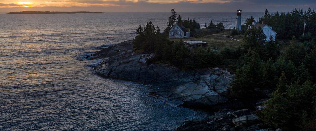 A coastal landscape with a lighthouse, rocky shoreline, and a small settlement with houses and trees.