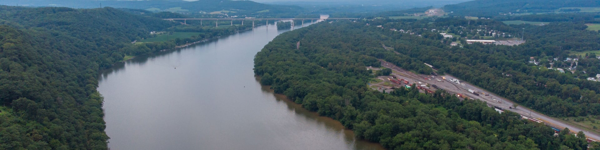 A river winding through a densely forested valley with a bridge in the distance.