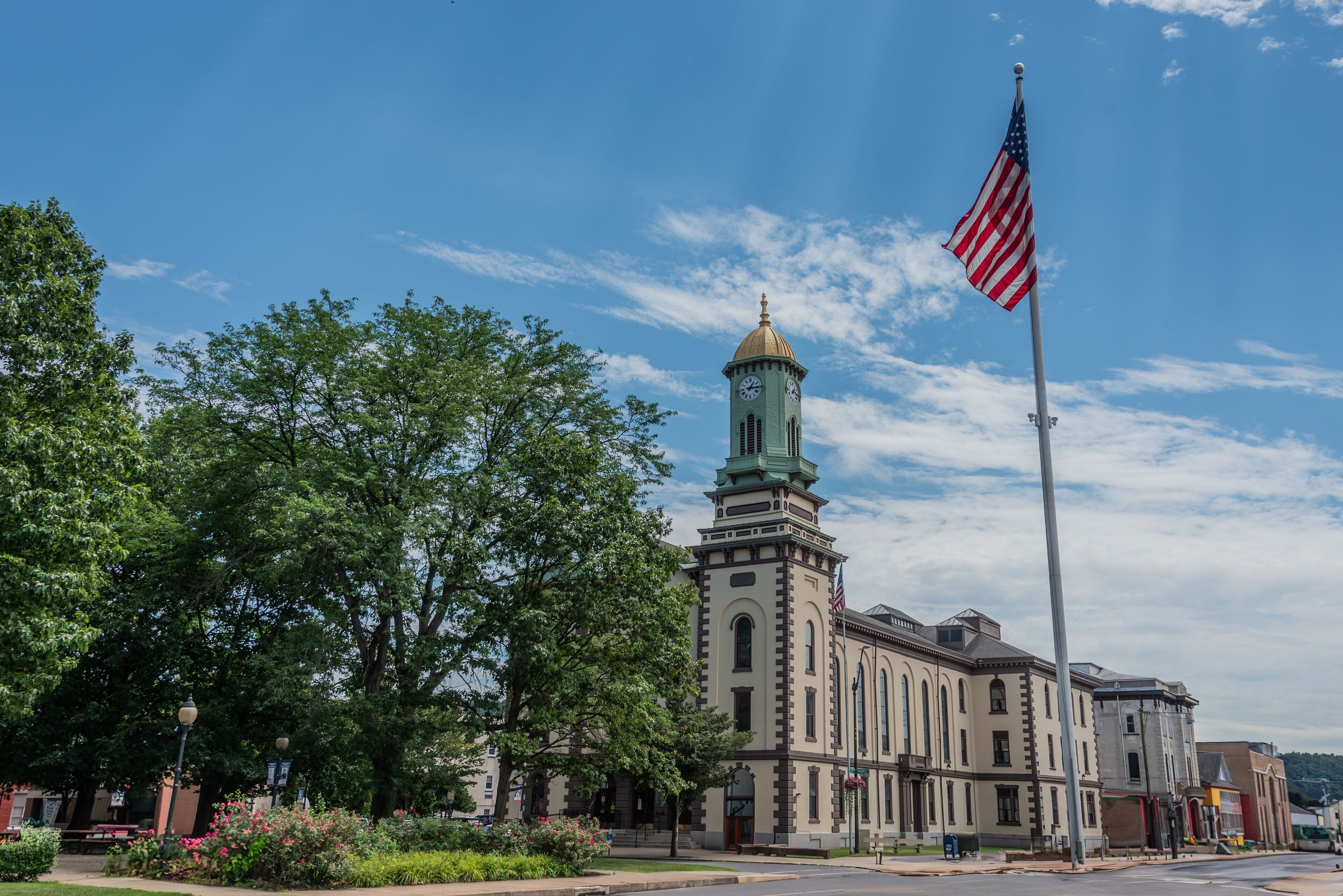 A historic building with a clock tower, surrounded by lush green trees and a flagpole with an American flag.