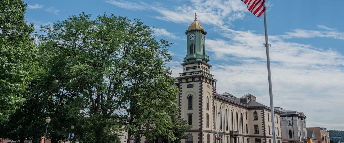A historic building with a clock tower, surrounded by lush green trees and a flagpole with an American flag.
