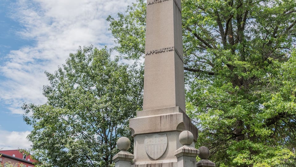 A tall monument with a statue on top, surrounded by trees and a clear sky.