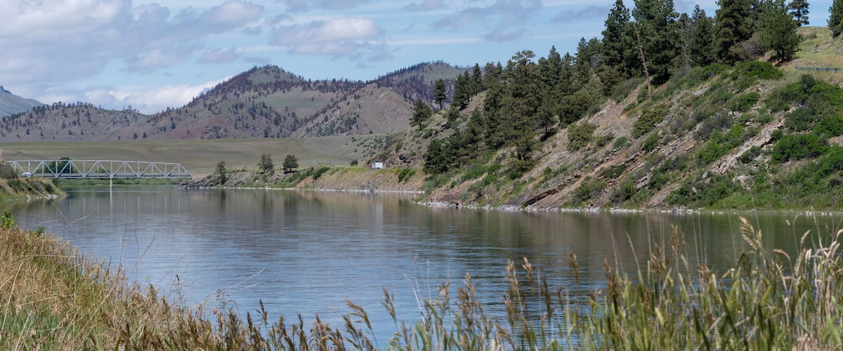 A calm lake with a bridge in the distance, surrounded by hills and trees.