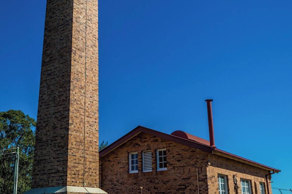 Um edifício de tijolos com uma chaminé alta e um grande barril de metal.
