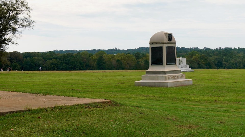 A grassy field with a large monument and a smaller structure with a dome roof.