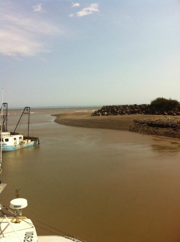 A calm river with a boat docked on the left, a rocky shoreline on the right, and a clear sky above.