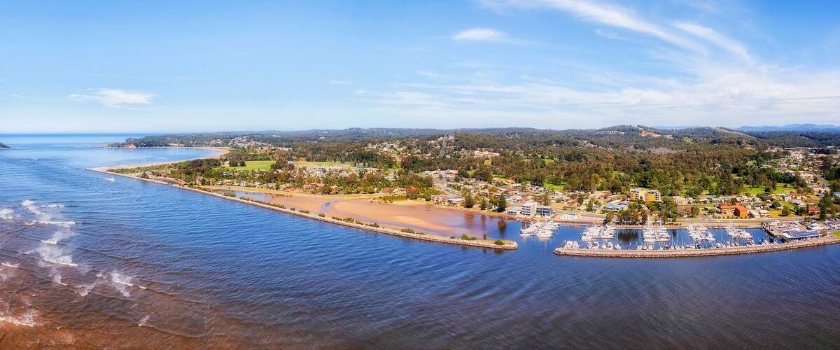 A coastal town with a marina, sandy beach, and surrounding hills.