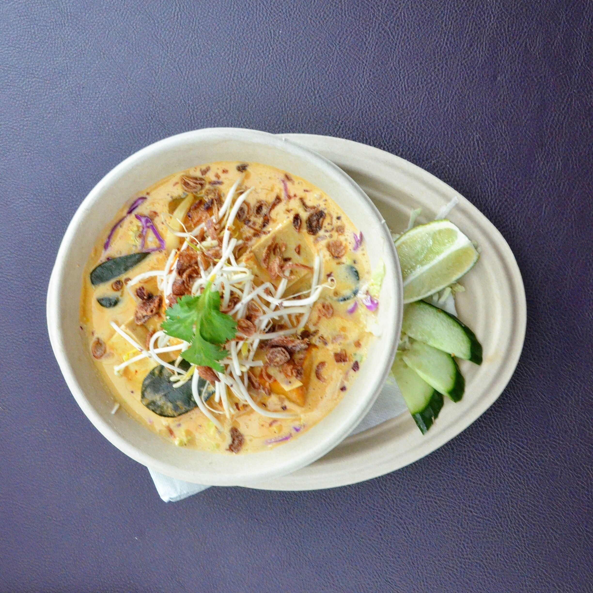 A bowl of soup with bean sprouts, cilantro, and lime wedges on a plate.