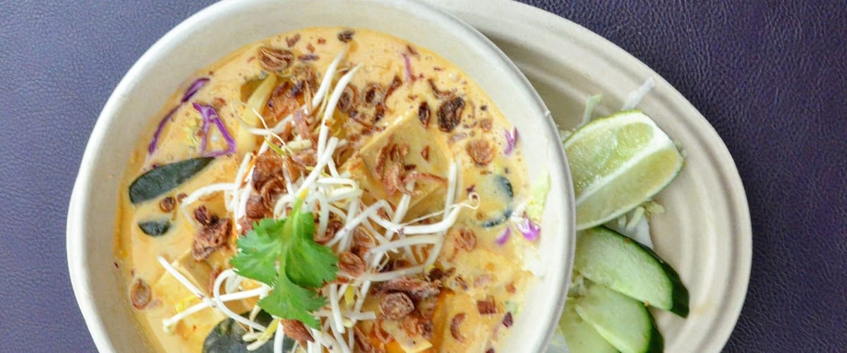 A bowl of soup with bean sprouts, cilantro, and lime wedges on a plate.