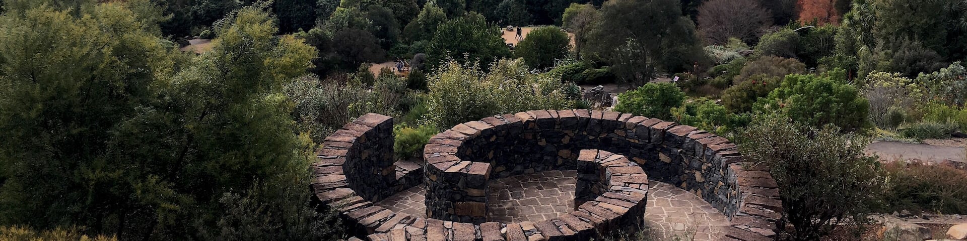 A stone spiral structure surrounded by dense forest and mountains in the background.