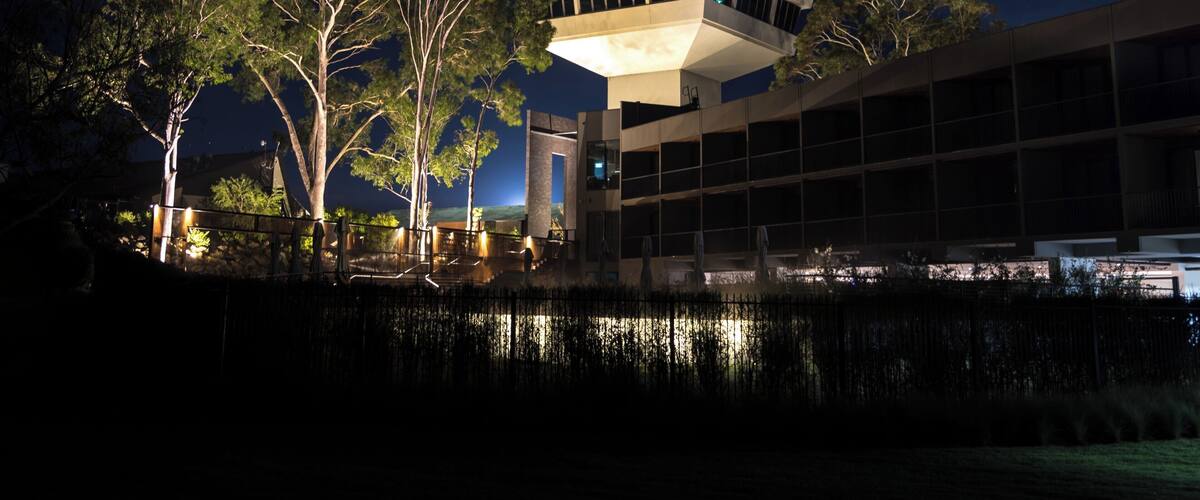 A modern building with a pyramid-shaped tower, surrounded by trees and a body of water.