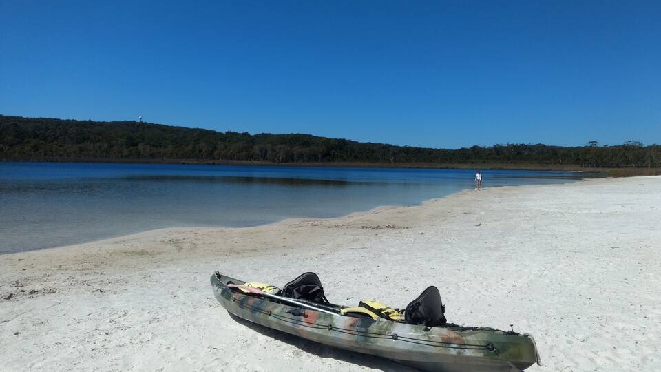 A kayak on a sandy beach with a person in the distance.