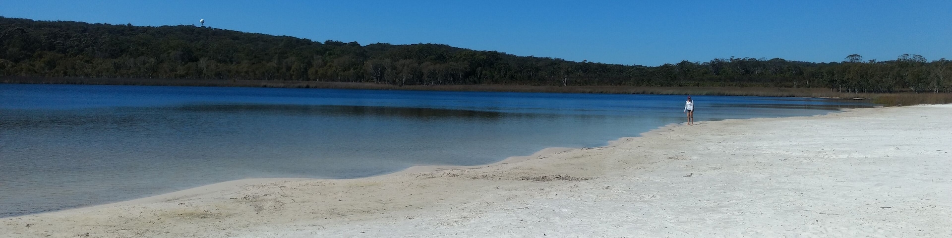 Un kayak en una playa arenosa, con una persona a lo lejos.