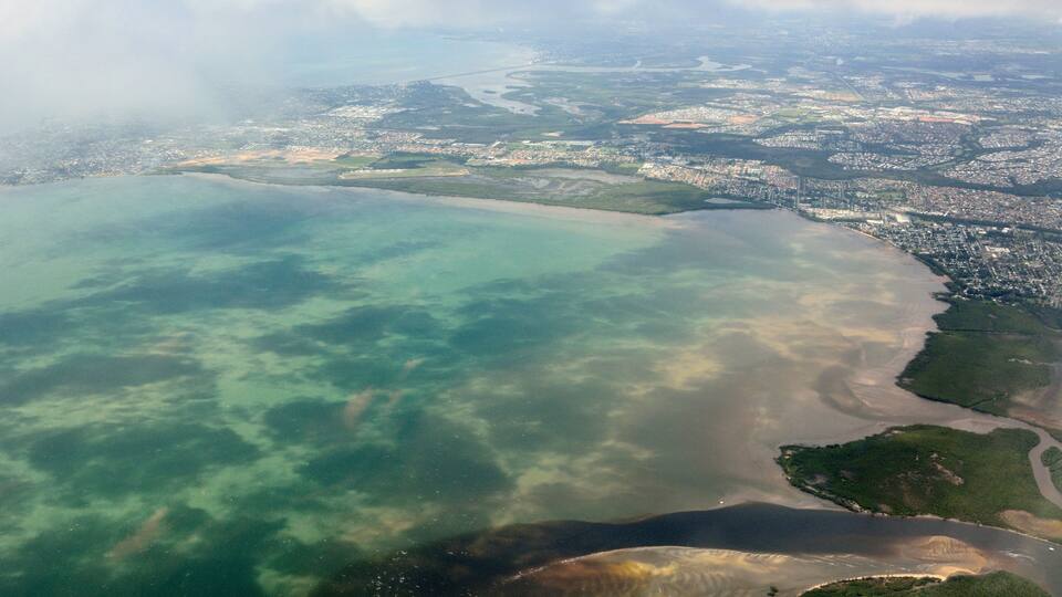 An aerial view of a coastal city with clear waters, a sandy beach, and urban areas.