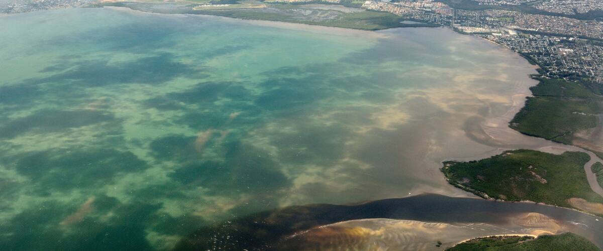 An aerial view of a coastal city with clear waters, a sandy beach, and urban areas.