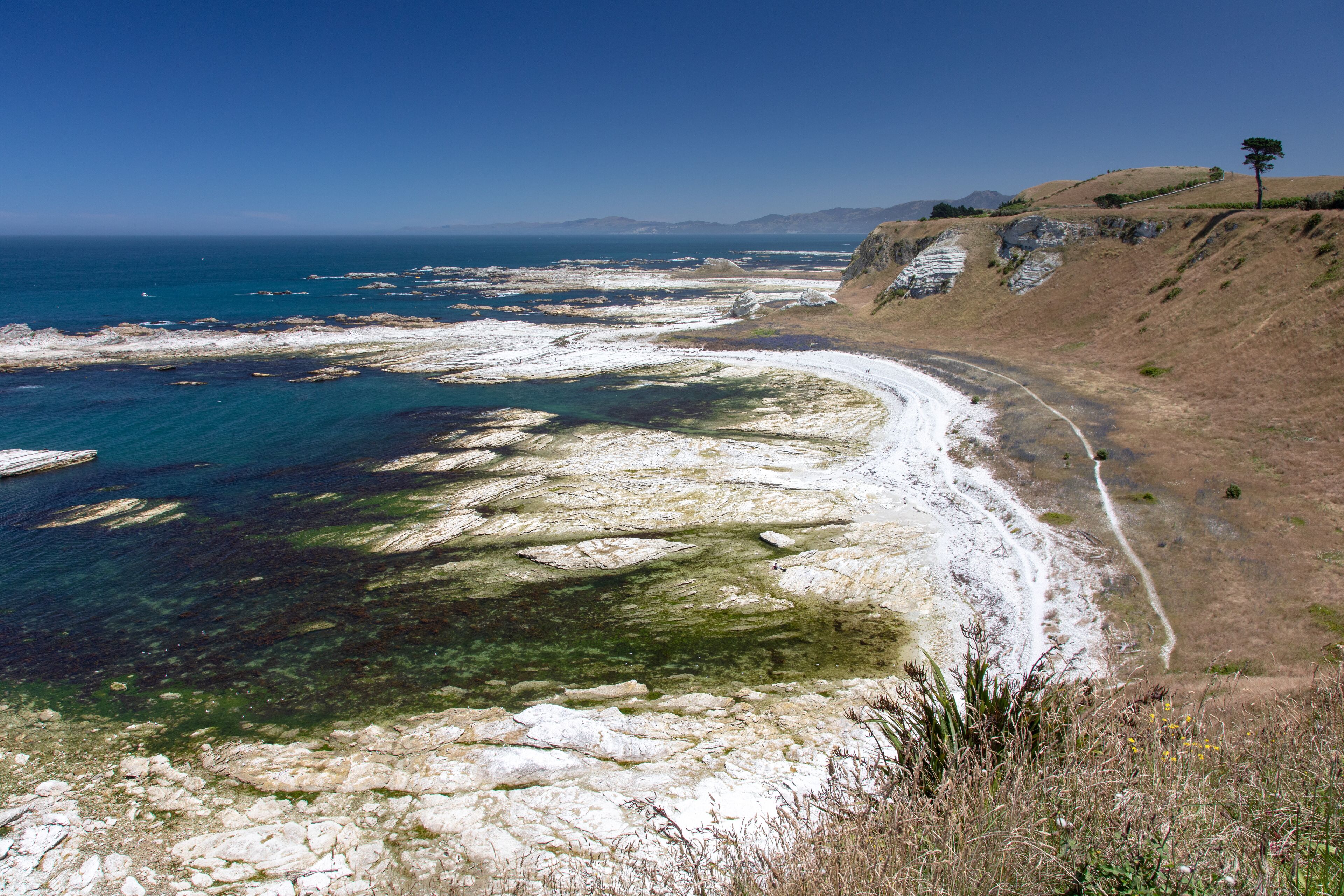A coastal landscape with clear blue waters, rocky shorelines, and a winding road along the coast.