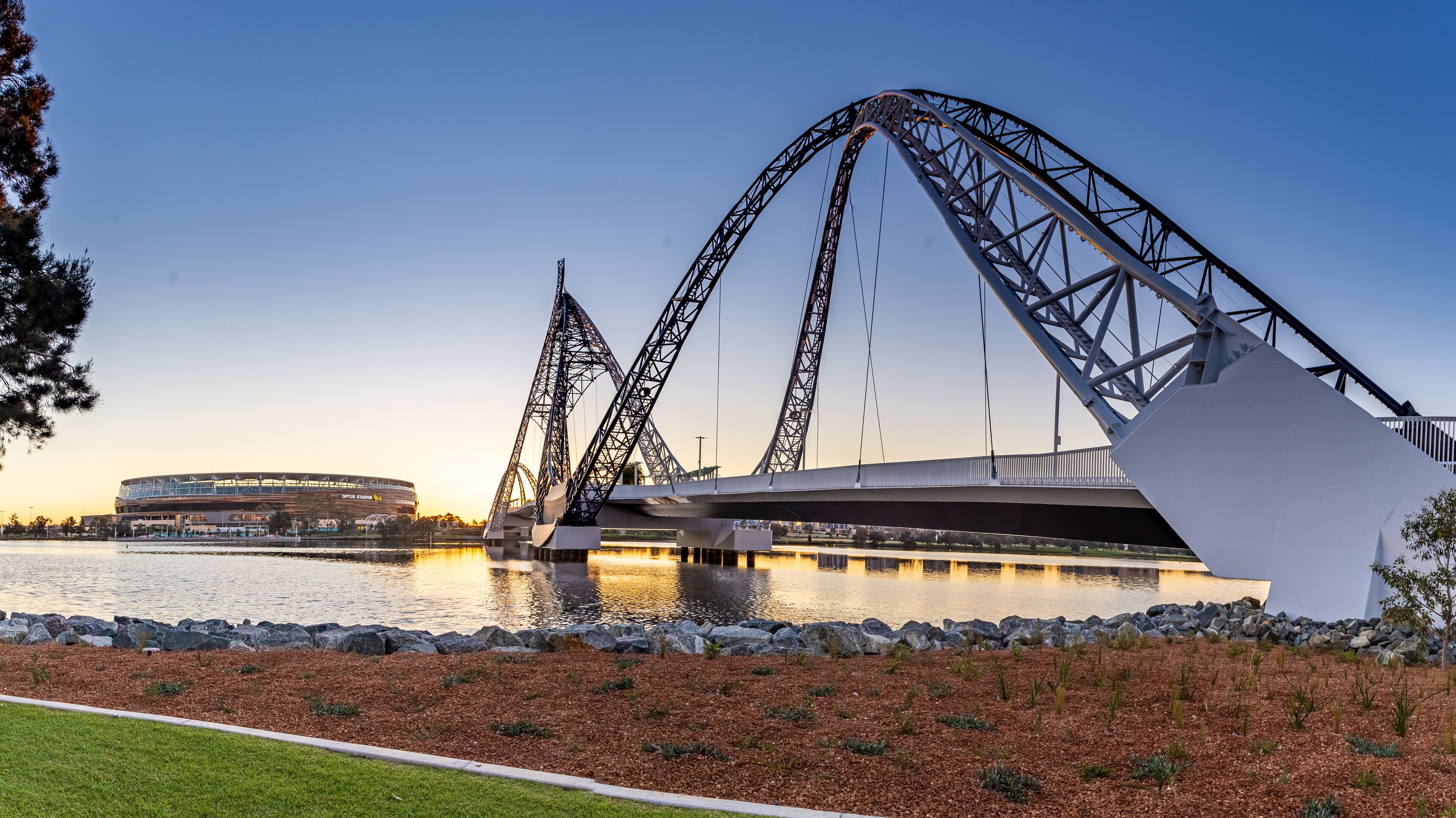 A roller coaster, a bridge, and a stadium by a body of water.