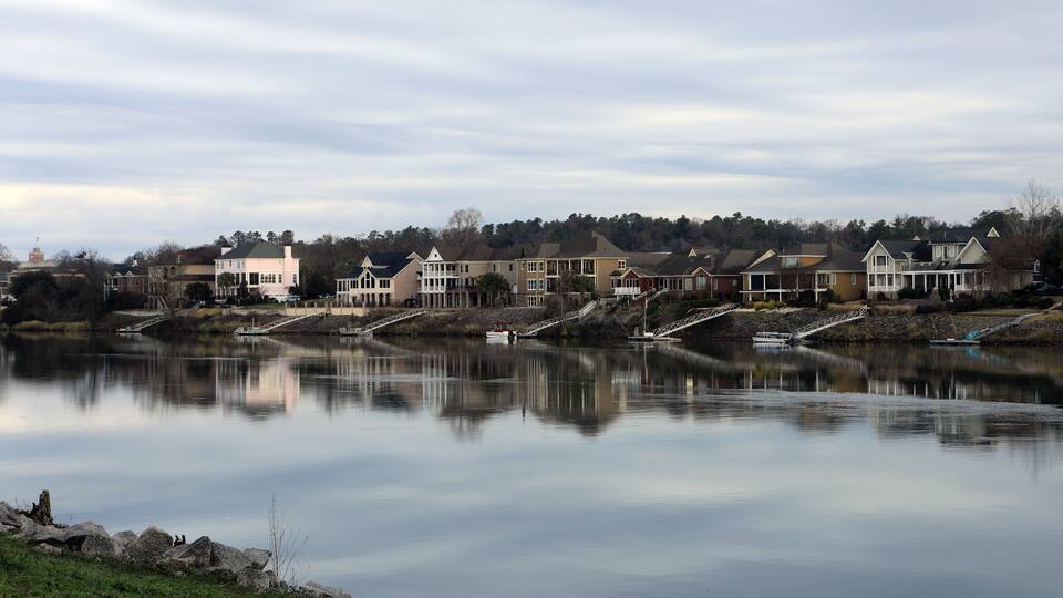 A calm lake with houses and a bridge.